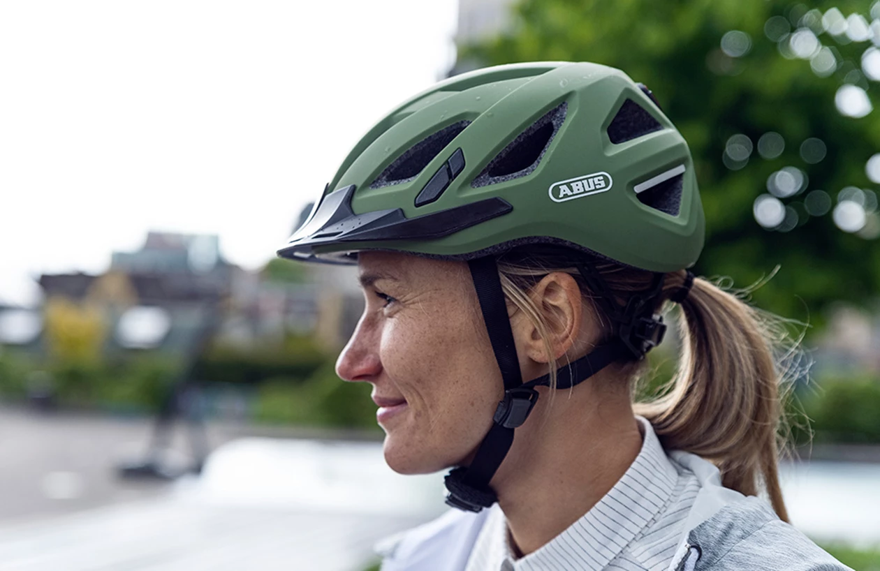 En kvindes sideprofil med grøn cykelhjelm med plads til hestehale
